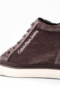 Baskets montantes en velours marron avec doublure intérieure noire, semelle beige, lacets à l'avant et "Calvin Klein Jeans" brodé sur le côté.