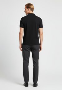 Černé polo tričko s krátkými rukávy, doplněné tmavě šedými kalhotami. Tkanina působí hladce, s designem úzkého střihu. Jednoduchý a klasický styl.