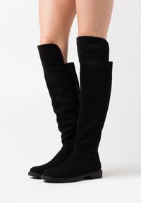 Botas de ante negro hasta la rodilla con una textura suave, punta redonda, suela de goma plana y diseño partido en la parte superior.