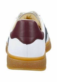 Bílá teniska s hnědým koženým krytem paty, černými pruhy po stranách a strukturovanou podrážkou v barvě dřeně. Viditelná měkká vnitřní podšívka.