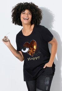 Mustat t-paidat, joissa on sydän- ja silmäkuvio, jotka on tehty paljeteista, ja joissa on sana "Happy" kullalla. Pehmeää kangasta, rento malli, yhdistettynä tummiin farkkuihin.