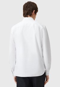 Hvid langærmet skjorte, knaplukning ved håndleddene, klassisk krave, buet kant, glat stofstruktur, med et rent, minimalistisk design.