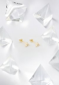Orecchini d'oro con tre gruppi di pietre come cristalli trasparenti, circondati da cristalli trasparenti a piramide sfaccettati su uno sfondo bianco.