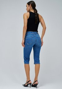 Vaqueros capri de mezclilla azul, ajuste slim con cinco bolsillos, cintura de altura media y dobladillo deshilachado. Combinados con una blusa sin mangas negra y tacones negros.