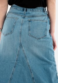 Leren spijkerrok in lichtblauw met een klokvorm, voorzien van twee achterzakken, een centrale naad en een middelhoge tailleband. Gladde textuur.