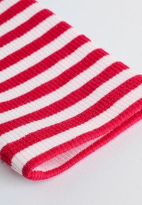 Primo piano di un tessuto piegato con righe orizzontali rosse e bianche e una texture a coste visibile su una superficie bianca.