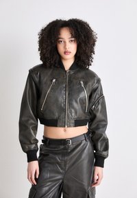 Biker-stil kort jacka i mörkt läder, med dubbla dragkedjefickor, ribbade ärmslut och en jämn yta. Kombinerad med matchande byxor.