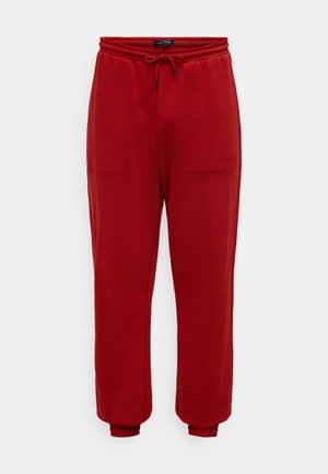 Pantalones deportivos rojos con cintura elástica, cordón ajustable, dos bolsillos delanteros y puños ajustados. Textura suave, diseño casual.