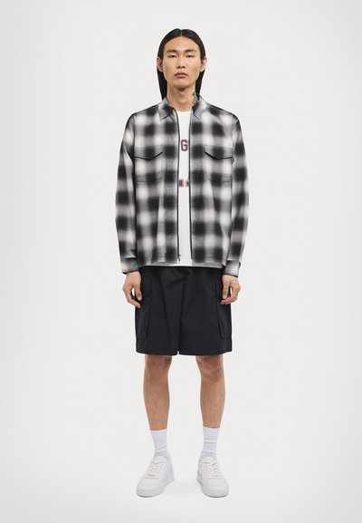 Black and white plaid zip-up shirt, two chest pockets, over a white T-shirt, paired with black cargo shorts and white sneakers.