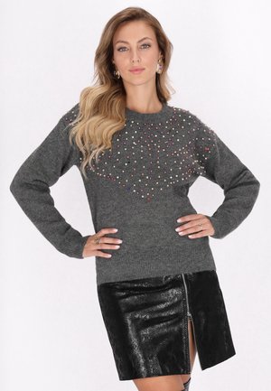 Pulover gri tricotat cu embellishments colorate în partea superioară, asortat cu o fustă neagră texturată cu fermoar.