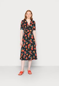 Vestido preto floral com mangas curtas, apresentando flores vermelhas e turquesas. Modelo a usar sandálias deslizantes vermelhas. O vestido tem um decote em V e um corte até meio da coxa.