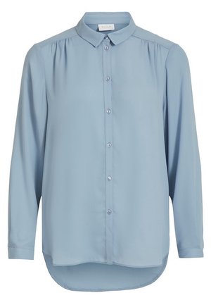 Blouse bleu clair à manches longues avec patte de boutonnage à l'avant, col classique, légers fronces aux épaules, et ourlet arrondi asymétrique.