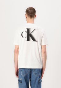 White cotton T-shirt featuring a large black "cK" logo on the back. Short sleeves and a classic crew neck design, relaxed fit.