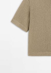 Beige ribbed short-sleeve top made of lightweight knit material, featuring a loose fit and subtle texture with a clean hem.