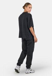 T-shirt noire oversized et pantalon de survêtement assorti en mélange de coton. L'ensemble présente une coupe décontractée et des poignets élastiques. Des baskets blanches complètent le look.