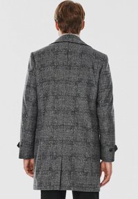Długi szary płaszcz w kratę z wyrazistym fasonem, dużymi klapami i zapięciem na guziki przy mankietach. Teksturowana tkanina o wzorze w kratę.