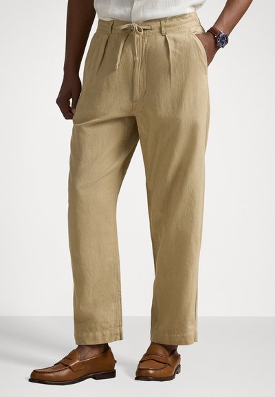 Beige pellaviseos housut rentoa karsintaa, naru vyötäröllä ja kaksi sivutaskua, yhdistettynä ruskeisiin loafer-kenkiin.