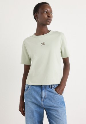 Lys grøn bomulds T-shirt med rund hals og korte ærmer, prydet med et lille rektangulært logo på brystet, båret med blå denim jeans.