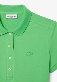 Polo vert en tissu texturé, avec un col classique, trois boutons et un logo brodé sur la poitrine.
