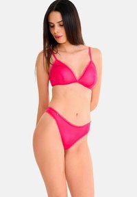 Ensemble de lingerie rose comprenant un bralette transparent avec des empiècements en dentelle et un string assorti. Les deux pièces présentent des accents délicats et une texture douce.