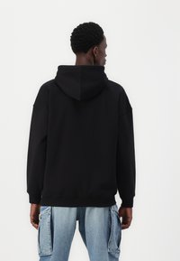Black hoodie with a large, adjustable hood. The fabric appears soft and thick, featuring dropped shoulders and ribbed cuffs.