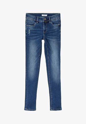 Jean slim bleu en denim avec une légère décoloration et un petit patch usé sur la cuisse droite, avec poches avant et fermeture à bouton.