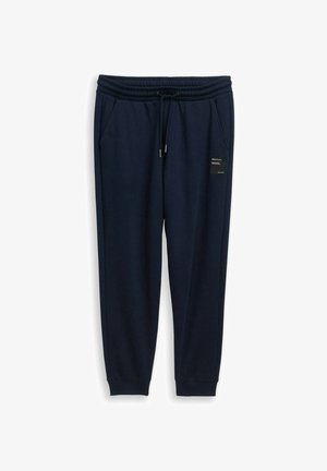 Dunkelblaue Jogginghosen mit elastischem Bund, Kordelzug, seitlichen Taschen, gerippten Bündchen und einem kleinen schwarzen Aufnäher am rechten Oberschenkel.