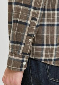 Brun og beige ternet flannelskjorte manchet med hvid knapdetalje, der har en blød tekstur og kontrasterende mørkeblå linjer.