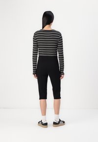 Svart och vitrandig långärmad topp med åtsittande svarta cropped byxor, kombinerat med svarta träningsskor och vita ankelsockor.
