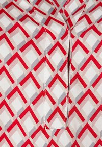 Tissu à motifs géométriques rouges, gris et beiges avec des formes rectangulaires ; présente une ouverture à patte au niveau du col. Texture lisse.