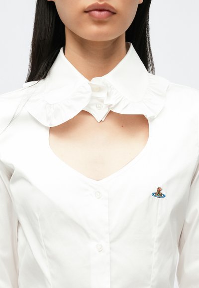 Camisa branca de algodão com gola franzida, decote em V e um pequeno desenho bordado no peito. Textura suave e ajuste estruturado.