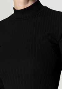 Top de cuello alto acanalado negro con un diseño ajustado, textura suave y un cuello simulado alto que acentúa la silueta.