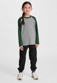 Grijze lange mouwen shirt met groene raglanmouwen, voorzien van een klein embleem. Gekozen met zwarte joggerbroeken en witte sneakers met groene accenten.