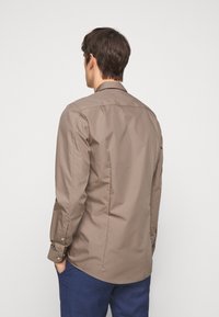 Brown button-up shirt with long sleeves, smooth texture, and a classic collar. Back view shows a tailored fit and side split hem.