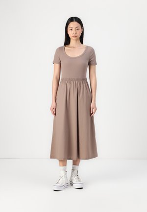 Midi-Kleid in Tan mit kurzen Ärmeln, einem Rundhalsausschnitt und einem elastischen Bund. Kombiniert mit weißen High-Top-Sneakern und Knöchelsocken.