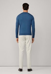 Blauer langärmeliger Pullover aus einem weichen Material, kombiniert mit cremefarbenen Hosen und schwarzen Schuhen, von hinten betrachtet.