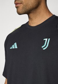 T-shirt noir à col rond, orné des logos turquoise d'Adidas et de la Juventus sur la poitrine et l'épaule. Tissu doux, manches courtes.