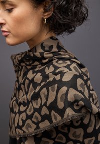 Läderskarf med leopardmönster i beige och svart, tillverkad av mjukt tyg med en texturerad finish. Har fransdetaljer längs kanterna.