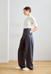 Top fitted grigio chiaro abbinato a pantaloni larghi grigio scuro a vita alta; tessuto morbido con tasche laterali e gambe ampie; abbinato a scarpe bianche.