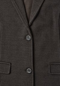 Blazer gris foncé motif chevrons avec deux boutons noirs et deux poches à rabat à l’avant.