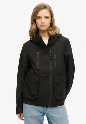 Veste à capuche noire avec fermeture éclair à l'avant, deux poches poitrine et deux poches à rabat à l'avant ; présente un logo subtilement embossé sur le devant.