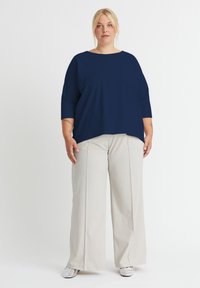 Marineblaues, locker sitzendes Oberteil mit Dreiviertelärmeln, kombiniert mit hoch-taillierten, weiten weißen Hosen und silbernen Schuhen.