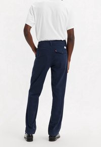 Pantalons en coton bleu marine avec une coupe droite, poches arrière, passants de ceinture et une petite étiquette logée sur la poche arrière.