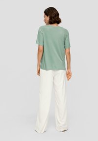 Lässig geschnittenes mintgrünes T-Shirt mit kurzen Ärmeln, kombiniert mit lockeren weißen Hosen; glatte Textur, schlichtes Design und Rundhalsausschnitt.