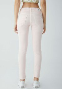 Světlé růžové úzké džíny s hladkou texturou, vybavené dvěma zadními kapsami a jemným švem, doplněné bílými teniskami.
