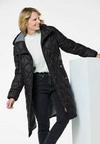 Zwarte gewatteerde pufferjas met capuchon, met een glanzende afwerking, ritssluiting en zijzakken. Gecombineerd met donkere jeans en een lichte top.