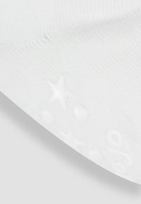 Weiße Socke mit strukturierter Oberfläche, die kleine erhabene Akzente in Form von Sternen und Kreisen an der Sohle für Grip und Design aufweist.