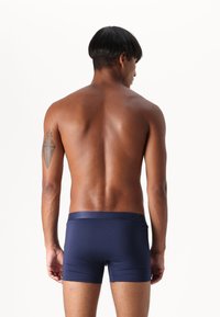Navy blue boxer shorts with a smooth texture and elastic waistband. The model is seen from the back, showcasing the underwear design.