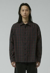 Checkered button-up shirt in dark navy and red pattern, featuring a spread collar, long sleeves, and a relaxed fit. Cotton material.