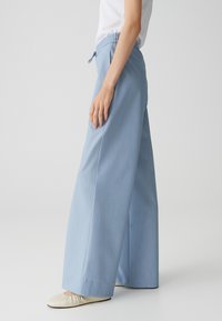 Pantalons larges bleu clair en tissu doux, avec une taille élastique et un cordon de serrage.